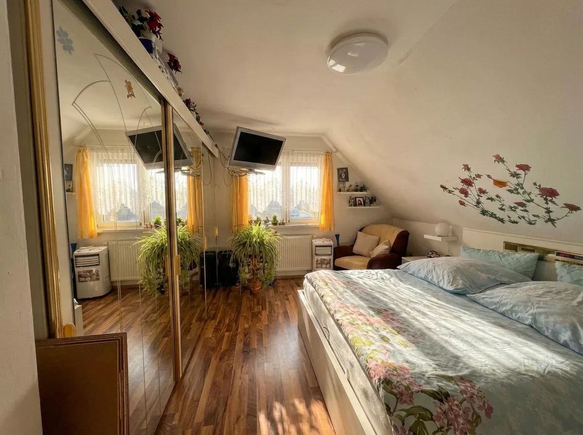 Schlafzimmer im Dachgeschoss mit Bett, Kleiderschrank, Fenster und Dachschräge.